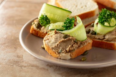 Bej tabakta ezmeli tost. Pate, taze salatalık, kapari ve maydanozlu sandviç..