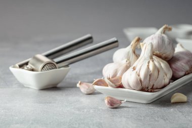 Garlic and garlic press on a grey stone table.