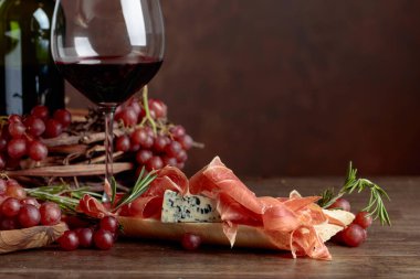 Prosciutto, mavi peynir ve koyu arkaplanda biberiyeli sandviç. Lezzetli aperatif ve kırmızı şarap. Metnin için boşluk kopyala.