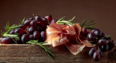 Eski ahşap bir tahtada üzümlü ve biberiyeli jambon..
