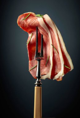 Sliced prosciutto with rosemary on a fork.