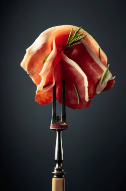 Sliced prosciutto with rosemary on a fork.