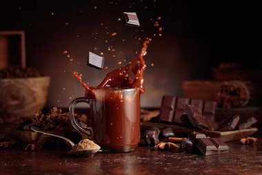 Kahverengi arka planda malzemeleri olan bir bardak sıcak çikolata. Kakao parçacıkları bir bardak kakao içeceğinin içine düşer ve güzel bir su sıçratır..