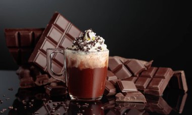 Krem şantili ve çikolata kırıntısı serpiştirilmiş sıcak çikolata. Arka planda kırık bir çikolata parçasında. Siyah yansıtıcı arka plan. Boşluğu kopyala.