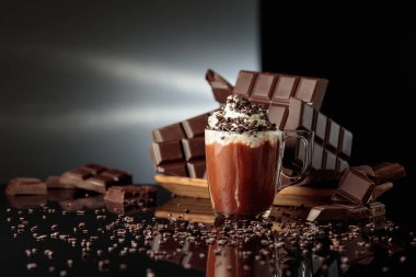 Çikolata kırıntıları serpiştirilmiş kremalı sıcak çikolata. Arka planda kırılmış acı çikolatalar. Siyah yansıtıcı arka plan. Boşluğu kopyala.