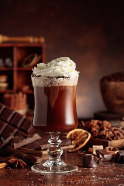 Cam bardakta krem şantili sıcak çikolata. Kahverengi arka planda malzemeleri olan çikolata içeceği..