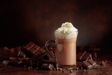 Krem şantili sıcak çikolata içeceği. Cam bardakta kakao ve koyu kahverengi arka planda acı çikolata..