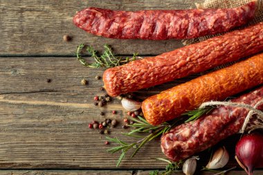 Various dry cured sausages with peppercorns, thyme, rosemary, onion, and garlic on a old wooden table. 