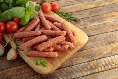 Sausages with basil and tomatoes on a cutting board.