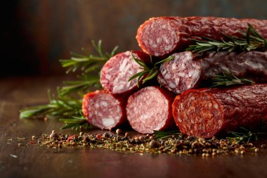 Smoked and dry cured sausages with rosemary and spices on a wooden table.