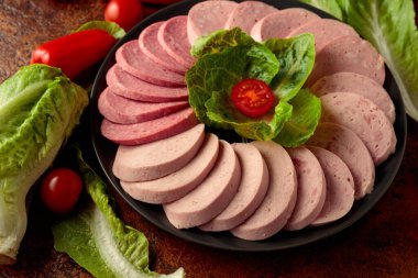 Various boiled sausages with greens and vegetables on a brown background.