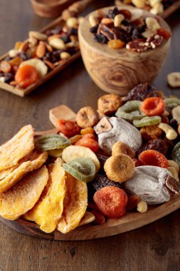 Kurutulmuş mango dilimleri, tropikal meyveler, fındıklar ve kuru üzümler eski ahşap bir masada..