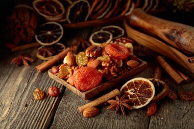 Eski ahşap bir masada kurumuş meyve ve fındık. Kurutulmuş turunçgiller, kayısılar, kuru üzümler, çeşitli fındıklar ve baharatlar..