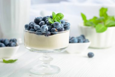 Beyaz ahşap bir masada taze yaban mersinli panna cotta. Nane şekeriyle süslenmiş çilekli parfüm..