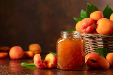 Kavanozda kayısı reçeli ve kahverengi bir masada taze meyve. Boşluğu kopyala.