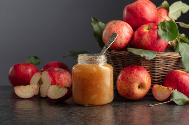Apple jam and fresh apples with leaves on a black background.