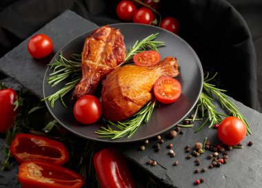 Smoked chicken drumsticks with greens and fresh vegetables on a black table.