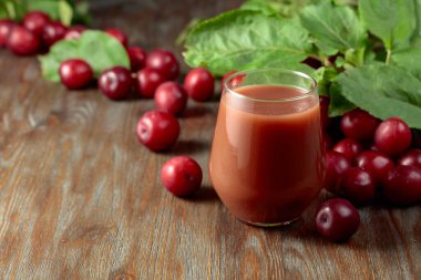 Red plums and a glass of plum juice on an old wooden table.