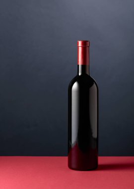 Bottle of red wine on a red table. Copy space.