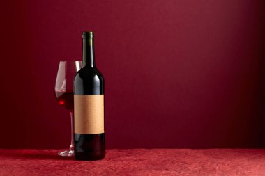 Bottle with old empty label and glass of red wine on a red background. Copy space.