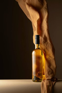 Bir şişe beyaz şarap ve koyu bir arkaplanda bej rengi kumaş..