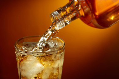 Buzlu bir bardağa dökülen bir şişe viski. Sıvı akış, canlı turuncu arka planda yakın plan görüntüsü yakalamış. Boşluğu kopyala.