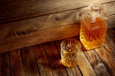 Zarif viski bardağı ve kehribar sıvısıyla dolu sürahi eski bir ahşap masada. Boşluğu kopyala.
