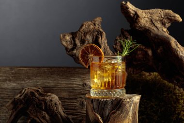 Eski moda bir kokteyl. Eski bir kütüğün üzerinde buz var. Kurutulmuş portakal dilimi ve biberiye dalıyla süslenmiş soğuk, ferahlatıcı bir içecek..