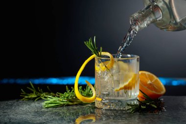 Limon ve biberiyeli cin tonik kokteyli. İçki şişeden buzlu bir bardağa dökülür. Boşluğu kopyala.