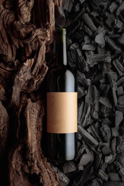 Bir şişe kırmızı şarap kömür ve kuru kaplara karşı. Zengin ve doygun dokuları olan kavramsal bir görüntü. Eski boş bir şişede.