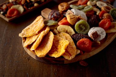 Kurutulmuş mango dilimleri, tropikal meyveler, fındıklar ve kuru üzümler eski ahşap bir masada..