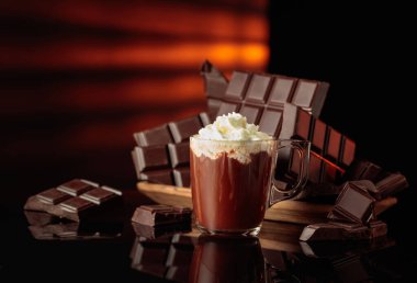 Kırık çikolatalara karşı krem şantili sıcak çikolata. Siyah parlak arka plan derinlik ve yansıma ekler. Boşluğu kopyala.