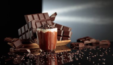 Çikolata kırıntıları serpiştirilmiş kremalı sıcak çikolata. Arka planda kırılmış acı çikolatalar. Siyah yansıtıcı arka plan. Boşluğu kopyala.