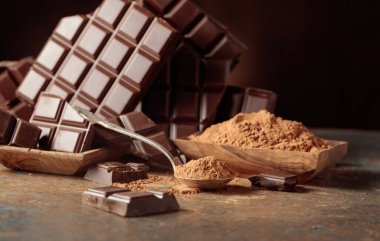 Kırık çikolata ve kahverengi arka planda kakao tozu. Boşluğu kopyala.