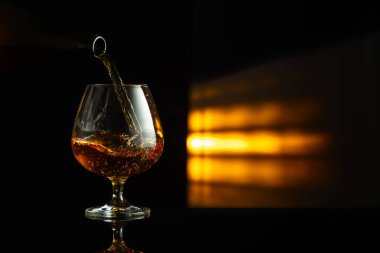 Bir şişeden siyah yansıtıcı arka planda bir bardağa brendi dökmek. Boşluğu kopyala.