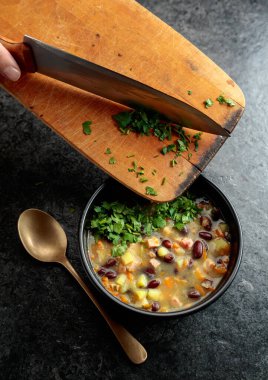 Siyah taş bir masada patates, domates, paprika, havuç ve pastırma ile kırmızı fasulye çorbası. Doğranmış maydanozu çorba kasesine serp..