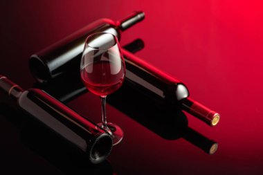 Siyah yansıtıcı arka planda cam ve kırmızı şarap şişeleri. Seçici odak.