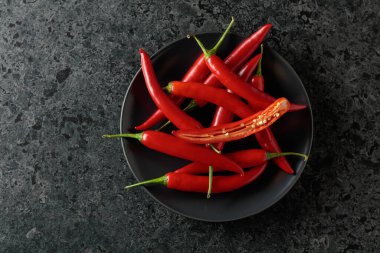 Siyah taş bir masada yeşil saplı taze kırmızı biber. Üst görünüm, alanı kopyala.