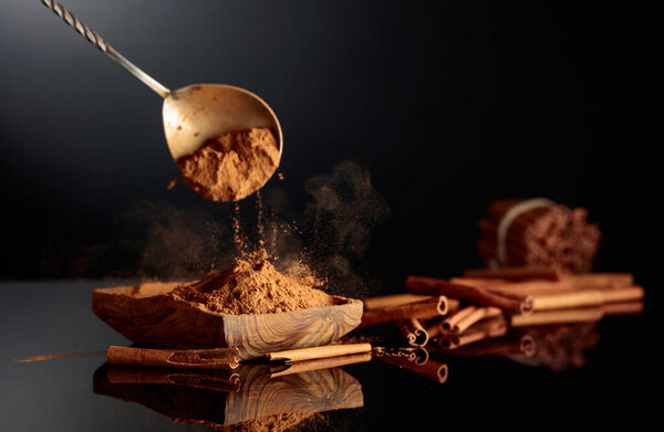 Порошок с корицей наливают в деревянное блюдо. Черный фон с местом для копирования.