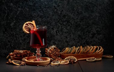 İçinde malzemeler olan sıcak şarap ve siyah bir mutfak masasında kuru portakal dilimleri. Boşluğu kopyala.