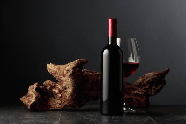 Siyah taş bir masanın üzerinde şişe ve bir bardak kırmızı şarap. Arka planda eski yıpranmış bir pürüz var. Kopyalama alanı ile ön görünüm.
