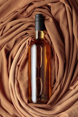 Bir şişe beyaz şarap örtülü bej ve kahverengi kumaştan oluşan bir arka plana karşı. Üst görünüm.