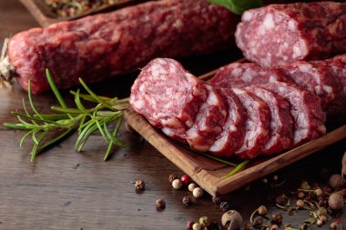 Ahşap bir masada baharat ve otlarla dilimlenmiş füme sosis..