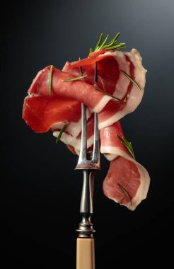 Sliced prosciutto with rosemary on a fork.
