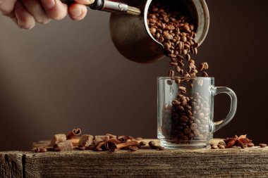 Kavrulmuş kahve çekirdekleri cam bardağa doldurulur. Eski ahşap bir masada anason, tarçın ve esmer şekerli kahve çekirdekleri. Kahve teması kavramı.