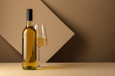 Bottle and glass of white wine on a beige background. Copy space.