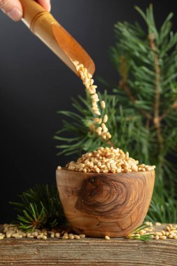 Çam fıstıkları ahşap bir kaseye dökülür. Soyulmuş çam fıstığı ve sedir dalı eski bir ahşap masada. Boşluğu kopyala.