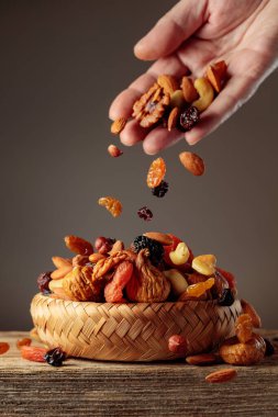 Kurutulmuş meyvelerin karışımı hasır bir kaseye dökülür. Kurutulmuş meyve ve fındık eski ahşap bir masada..