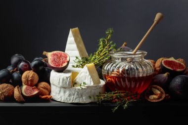 İncirli, üzümlü, cevizli, ballı ve kekikli Camembert peyniri. Siyah arka planda meyveli yumuşak peynir..