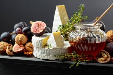 Siyah arka planda meyveli yumuşak peynirler. İncirli, üzümlü, cevizli, ballı ve kekikli Camembert peyniri..